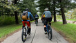 © .shock - Group mountain bikers riding on a tree-lined paved park path with backpacks and helmets