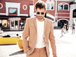 © halayalex - Handsome confident stylish hipster lambersexual model.Sexy modern man dressed in elegant beige suit. Fashion male posing in the street background in Europe city at sunset. In sunglasses