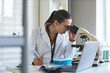© DragonImages - Young adult Caucasian woman scientist examining sample through microscope and taking notes in laboratory. Ideal for medical research, biotech innovation, diagnostics marketing