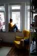 © Westend61 - Woman sitting on a windowsill at home using a smartphone and drinking tea