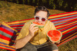 © Westend61 - Man eating watermelon and relaxing in hammock on summer day