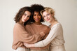 © Ekaterina - Three young women embracing and smiling in neutral outfits indoors