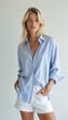 © Maryna - Slim woman in light blue striped shirt and white shorts poses confidently. Hands in pockets, she looks at camera against plain studio backdrop. Casual elegant attire.