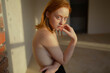 © Westend61 - Red-haired woman with freckles indoors in sunlight looking at camera