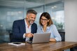 © tino - Professional colleagues collaborating in a modern office space, focusing on a laptop. Bright glass windows create a clean and open atmosphere.