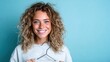 © svastix - A happy young woman beams confidently while holding a clothing hanger, showcasing her vibrant personality against a bright turquoise background, perfect for fashion themes.