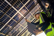 © ultramansk - Technician inspects solar panels under a large solar carport structure. Focused on clean energy, and sustainability, Engineer in safety vest and helmet pointing towards a solar powered carport.