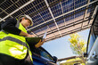 © ultramansk - Engineer in safety vest and helmet pointing towards a solar powered carport, illustrating eco-friendly innovation in parking infrastructure. Solar panels provide shade and sustainable energy.