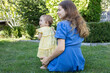 © Anna - woman in a blue dress and a baby girl in a yellow dress sitting on the grass on a summer day. The closeness of mother and daughter, caring for a small child. A pleasant moment of motherhood