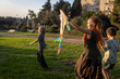© elenarostunova - An artistic wide shot on green grass in a park. A small child's back is to the camera, and the adult woman with dreadlocks is flying a large, colorful kite, partially obscuring the girl.