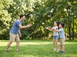 © SoloPixel - Asian Father Playing Catch with Children in Green Park on Sunny June Day