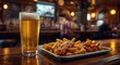 © TheWaterMeloonProjec - Sparkling beer poured in a glass next to a fast food snack assortment on a bar table at a lively sports bar
