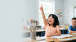 © Alena Yakusheva - Cheerful girl raising her hand and pointing up during a lesson in a bright classroom, active involvement, inclusive primary education, student life.