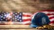 © A5 - Blue plastic construction hard hat and yellow leather work gloves on a textured wooden table with a blurred American flag background and soft light rays illuminating the scene.