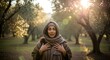 © samiya - Woman wearing a brown headscarf and shawl, standing in an olive grove with soft golden sunlight filtering through the trees