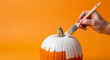 © Sarah - Close up of a hand painting a fresh pumpkin white on orange perfect for creative autumn DIY decorations
