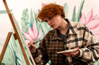 © Cavan - A red-haired girl artist paints on an easel.