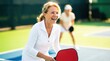 © Hypnyo - Happy senior woman playing pickleball on sunny outdoor court. Active retirement lifestyle and recreational sports for healthy older adults.