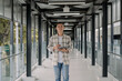 © Rijjal - Smiling asian man holding tablet in a modern glass hallway.  working online.  Work from anywhere. modern tech