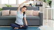 © snowing12 - Asian woman adult doing yoga side bend stretch on mat at home living room maintaining healthy lifestyle fitness wellness exercise indoors calm mindful practice