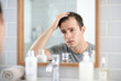 © Meow Creations - Concerned man touching thinning hair while looking in bathroom mirror