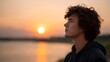 © Thares2020 - A thoughtful man stands by a calm body of water bathed in the warm golden light of the setting sun