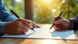 © Vadym - Close-up hands sign agreement papers on wooden table. Sunlight streams in, illuminating partnership deal. Business partners finalize contract, make decision, plan future strategy for success.