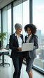 © Vadym - Two businesswomen talk about laptop computer in office. Women smile, look at screen. Diverse colleagues in modern workspace discuss project. Teamwork, partnership shown. Corporate meeting happens.