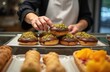 © Vadym - Baker arranges chocolate frosted donuts topped with pistachios in shop display. Fresh baked goods ready for sale at pastry counter. Variety of sweets offered.