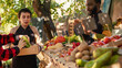 © DC Studio - Senior man and young woman buying organic bio products, visiting local farmers market stand. Smiling vendors greeting customers and selling homegrown fruits and veggies from farm.