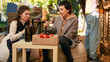 © DC Studio - Team of women at harvest festival tasting organic wine, sitting next to local farmers market stand. Customer and farmer drinking fresh natural bottle of homemade wine, products sampling.