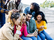 © Xavier Lorenzo - Group of diverse millennial friends enjoying time together outdoors while using mobile phones. Friendship, connection and social lifestyle concept.