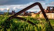 © Tania - Twisted and corroded rusty metal frame lying amongst overgrown weeds and distant industrial wreckage under a dramatic sky.