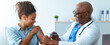 © Prostock-studio - A woman sitting in a clinic smiles as a doctor administers a vaccine to her arm. The doctor wears a stethoscope and looks professional. Soft light fills the room.