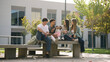 © DMegias - Group of young college students sitting on a bench outside university building, communicating and studying together during break
