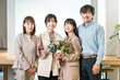© buritora - A smiling businesswoman receives a bouquet of flowers, while her team members applaud.