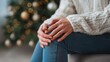 © Batagor - A person sits thoughtfully with their hands clasped, a cozy sweater and blurred Christmas tree lights creating a warm and introspective atmosphere.