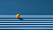 © Api - A single orange rests on a textured blue surface, creating a striking contrast of color and form.