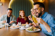 © djile - Man eating sandwich with friends enjoying meal together in cafe