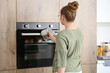 © Pixel-Shot - Woman opening electric oven with buns in kitchen