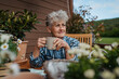© Halfpoint - Senior woman with coffee sitting on terrace, resting after gardening.