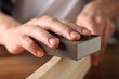 © New Africa - Man polishing wooden plank with sanding block at table, closeup