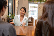 © Jestercine - Charismatic young Asian businesswoman in a mint blazer speaks confidently to colleagues during an informal business meeting at café.