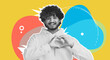 © Prostock-studio - A young man is smiling while making a heart gesture over his chest. He wears a yellow hoodie and stands in front of a bright yellow background with colorful shapes.