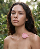 Editorial portrait of a woman with luminous skin, single fresh rose petal resting on her collarbone, dewy glass skin finish, full lips in nude gloss, soft wavy dark hair loose