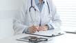 © volha_r - Female doctor documents patient information while working with digital devices at minimalist white workstation in medical office. Medicine and healthcare concept