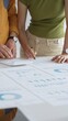 © rogerphoto - Two business professionals are collaborating on a project, analyzing financial charts and statistics displayed on a table, using a calculator for precise calculations. close up vertical view