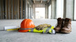 © solom - Construction personal protective equipment including orange hard hat safety vest boots goggles gloves and blueprints on concrete floor of building site under development