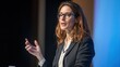 © David - A confident businesswoman in a black blazer and glasses giving a presentation on stage with a blue background