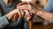 © twilight mist - Compassionate caregiver holds the hands of an elderly person resting on a wooden walking cane.